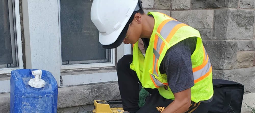 man in hard hat and vest working taking samples outside a building.