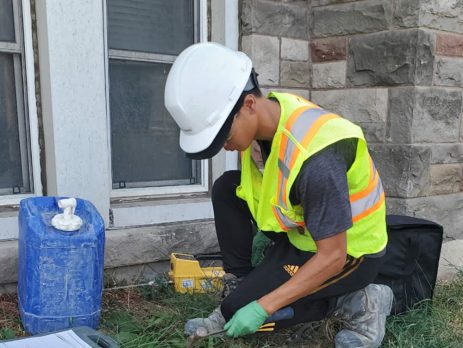 man in hard hat and vest working taking samples outside a building.