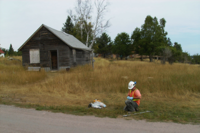 Image of worker in a field, next to a small older wood building, conducting property analysis.