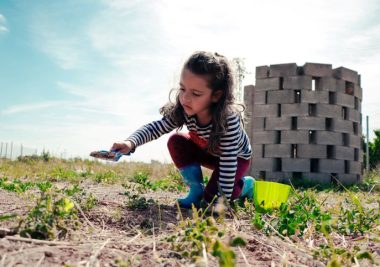 Image of young child playing in a field with construction blocks behind her.