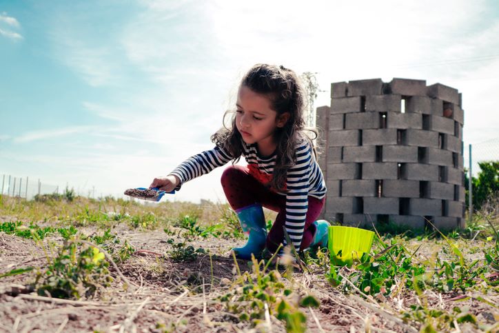 Image of young child playing in a field with construction blocks behind her.