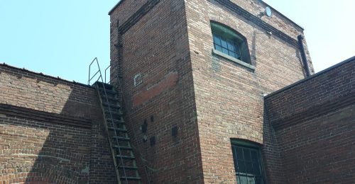 Face of brick abandoned factory building with a metal latter going to the roof.